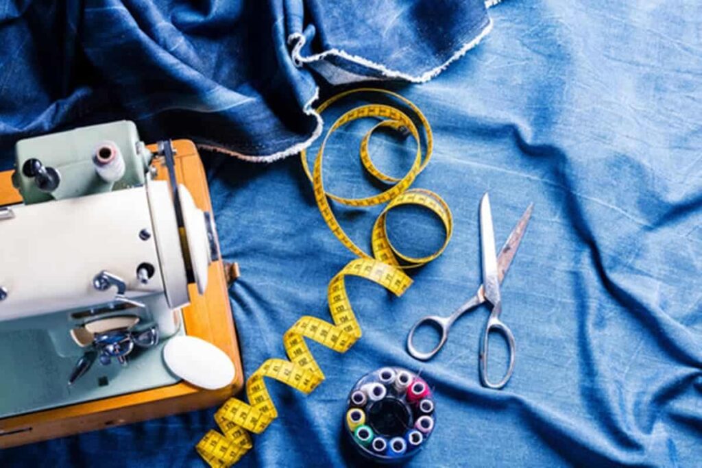 A imagem apresenta um conjunto de ferramentas e materiais comumente utilizados em costura e conserto de roupas dispostos sobre um tecido jeans. Os elementos visíveis são: Máquina de costura: No centro da imagem, uma máquina de costura antiga, de cor creme, com detalhes em metal. A máquina está posicionada sobre o tecido jeans, com a parte superior aberta, revelando o mecanismo interno. Tecido jeans: Um grande pedaço de tecido jeans azul escuro serve como fundo para a imagem. O tecido está dobrado e amassado, criando uma textura visualmente interessante. Tesoura de costura: Uma tesoura de costura de metal, com pontas afiadas e anéis para os dedos, está posicionada sobre o tecido jeans, próxima à máquina de costura. Fita métrica: Uma fita métrica amarela, enrolada em espiral, está posicionada ao lado da tesoura. A fita métrica é um instrumento essencial para medir tecidos e garantir precisão nas costuras. Carretel de linhas: Um carretel de linhas coloridas está posicionado ao lado da fita métrica. O carretel contém várias bobinas de linha de diferentes cores, prontas para serem usadas na máquina de costura. A imagem transmite uma sensação de tradição e artesanato, evocando a ideia de um ateliê de costura. Os elementos visuais são ricos em detalhes e a composição da imagem é harmoniosa, criando uma atmosfera acolhedora e convidativa. Elementos adicionais que podem ser mencionados: Iluminação: A imagem é bem iluminada, com uma luz suave que destaca as texturas e as cores dos objetos. Profundidade de campo: A imagem possui uma profundidade de campo relativamente rasa, com a máquina de costura e os objetos próximos em foco nítido, enquanto o fundo do tecido jeans está ligeiramente desfocado. Composição: A composição da imagem é simétrica, com os objetos dispostos de forma equilibrada em torno do centro. Possíveis interpretações da imagem: A imagem pode ser interpretada de diversas maneiras, dependendo do contexto e da perspectiva do observador. Algumas possíveis interpretações incluem: A paixão pela costura: A imagem pode representar a paixão pela costura como um hobby ou profissão. A tradição da costura: A máquina de costura antiga e os materiais tradicionais evocam a ideia de uma tradição que se mantém ao longo do tempo. A criatividade: A variedade de cores e texturas dos materiais sugere a possibilidade de criar peças únicas e personalizadas. O trabalho manual: A imagem valoriza o trabalho manual e a importância de cada detalhe na confecção de uma peça de roupa. Em resumo, a imagem apresenta um conjunto de elementos que se relacionam com a prática da costura, transmitindo uma sensação de tradição, criatividade e trabalho artesanal. A composição visualmente atraente e os detalhes ricos convidam o observador a explorar o universo da costura e a apreciar a beleza dos objetos e materiais utilizados nesse ofício. Palavras chave: conserto de roupas em goiania, ajuste de roupas