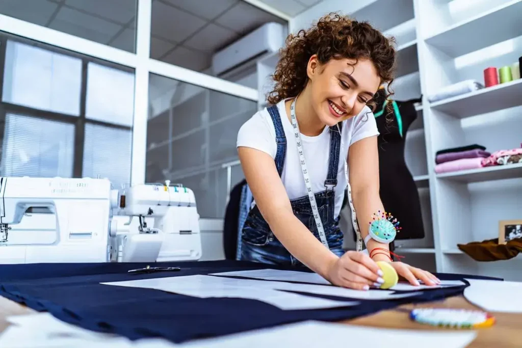 Costureira sorridente ajustando tecido em ateliê organizado, mostrando serviço profissional de reformas de roupas em Goiânia.